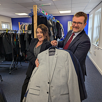 Faye Mellors (left) and Matthew Wells (right) smiling holding suit jackets.