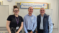 A female and two males stood in a line smiling in front of a Premier Learning sign