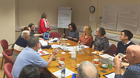 A group of adults sat around a table looking at a flip board with writing