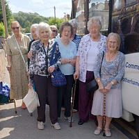 A group of older women stood by a community transport bus