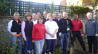 A group of people stood in an allotment setting with some holding gardening equipment