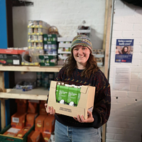 A woman smiling into the camera and is holding a food package 