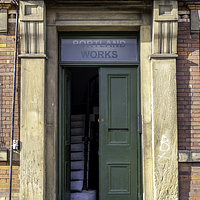A clos eup image of the entrance to the Portnalnd works, a green double door against a red brick building. On the top of the door there is a panel of frosted glass that says ' the portland works"