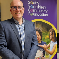 A male adult stood smiling in front of an SYCF banner