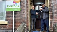 Two men stood by a sold sign shaking hands and exchanging keys