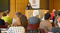 A lady stood behind a lectern addressing an audience